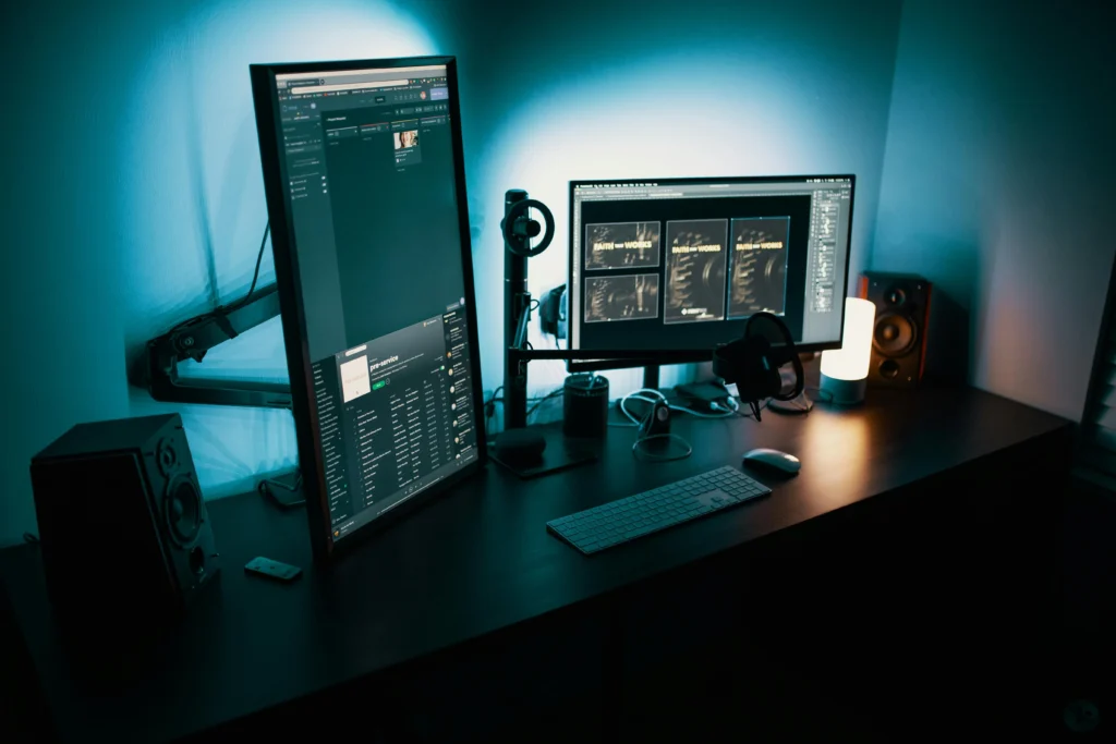 Nano Banana vs. Photoshop vs. Midjourney: Which Image Editing Tool Dominates Real-World Creative Needs? Modern desk setup with a vertical and a widescreen monitor, keyboard, headphones and speakers in teal ambient light—used for AI photo-editing workflows.
